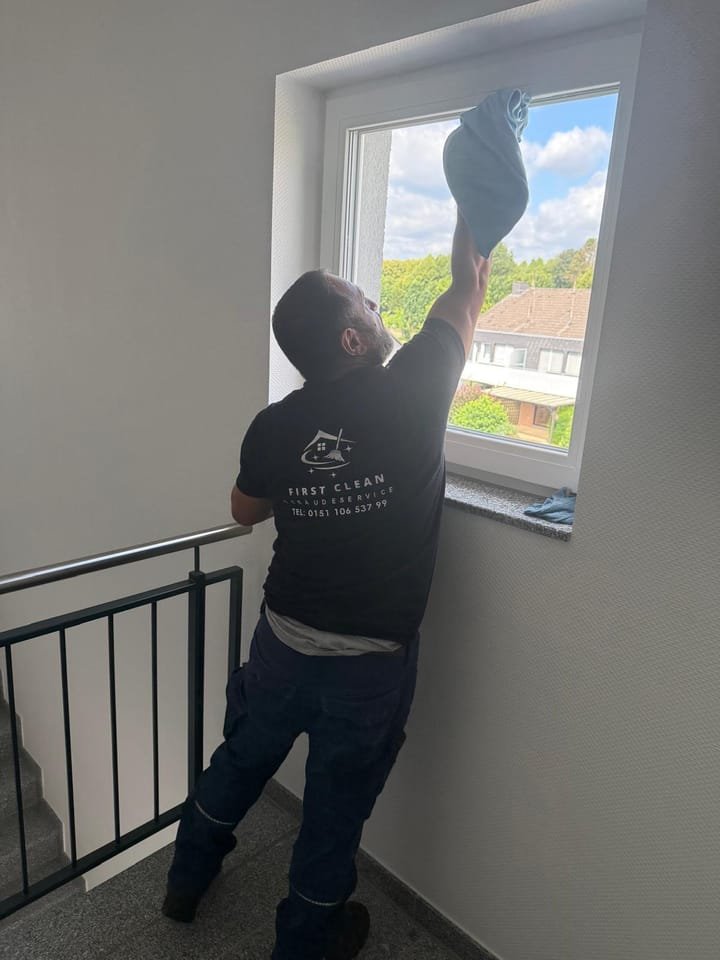 Mitarbeiter von First Clean reinigt ein Treppenhausfenster mit Mikrofasertuch