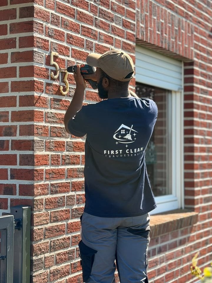 Mitarbeiter von First Clean montiert eine Hausnummer an der Klinkerfassade eines Wohnhauses
