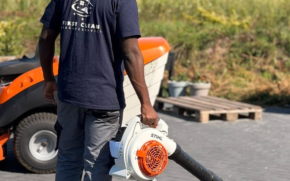 Mitarbeiter von First Clean reinigt eine gepflasterte Hoffläche mit dem Laubbläser