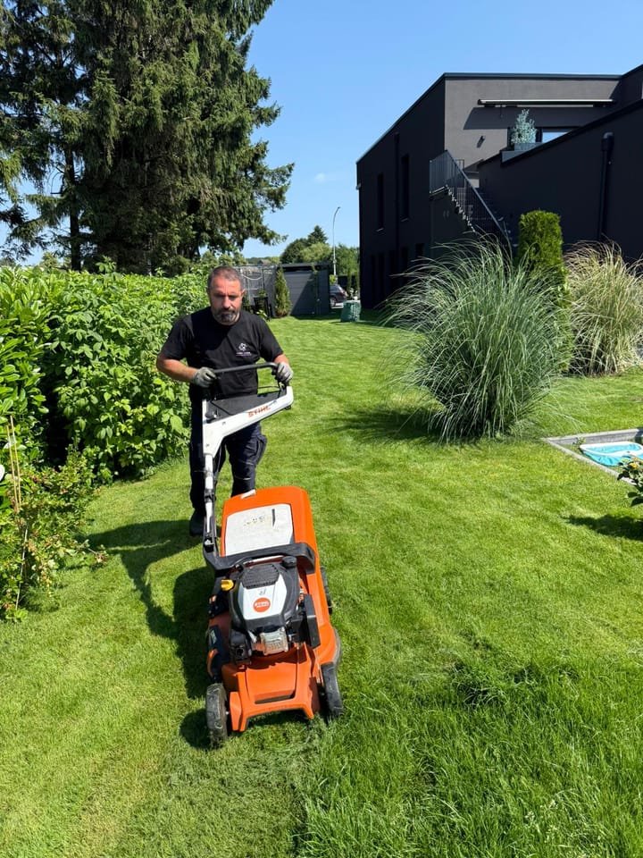Mitarbeiter von First Clean mäht den Rasen einer gepflegten Gartenanlage