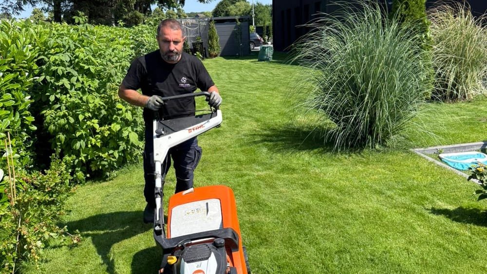 Mitarbeiter von First Clean mäht den Rasen einer gepflegten Gartenanlage