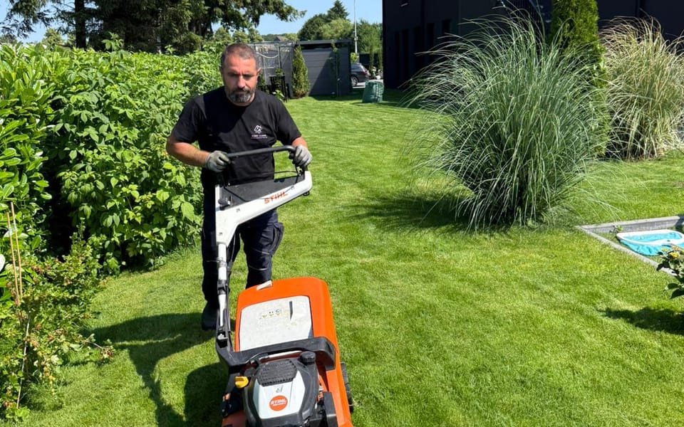 Mitarbeiter von First Clean mäht den Rasen einer gepflegten Gartenanlage